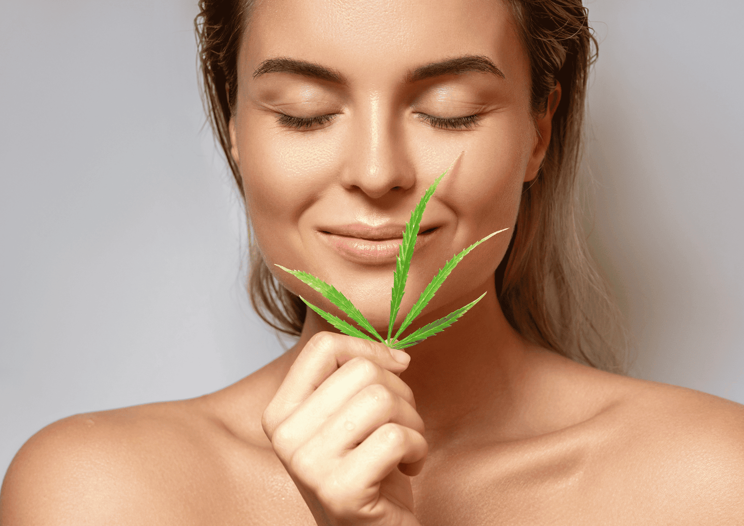 Frau hält Cannabisblatt vor das Gesicht und grinst