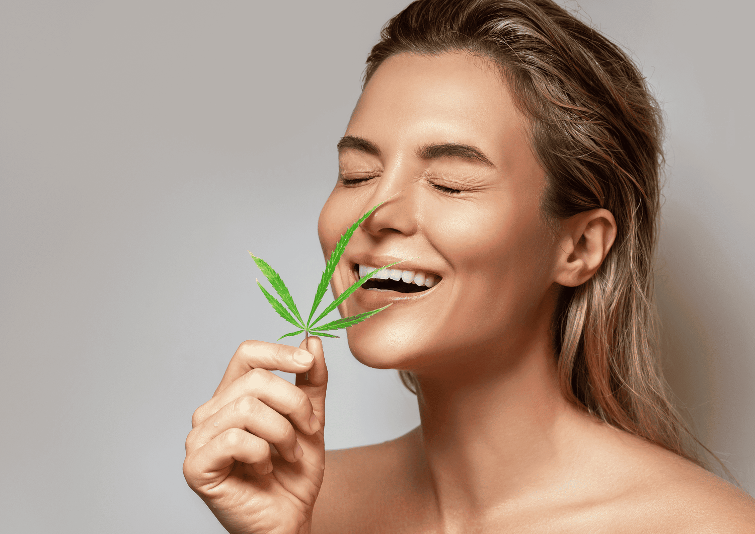 Frau hält vor ihr Gesicht ein Cannabisblatt, hat die Augen zu und lächelt