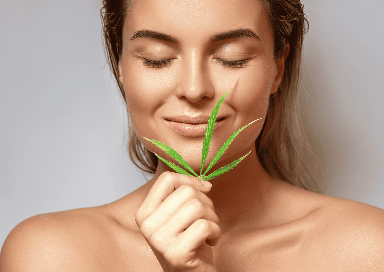 Frau hält Cannabisblatt vor das Gesicht und grinst